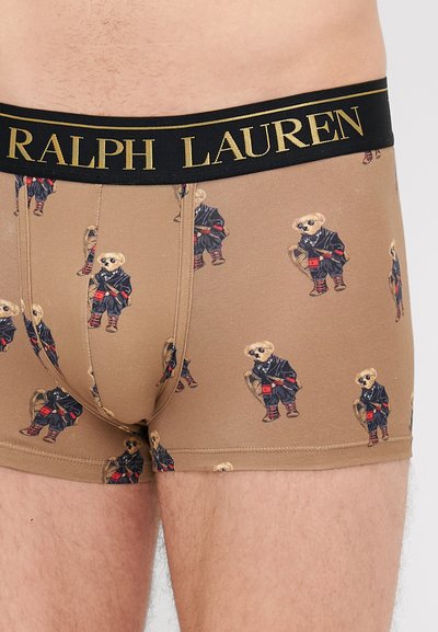 Brązowe slipki z powtarzającym się wzorem niedźwiedzi ubranych w garnitury. Czarny pas z nadrukiem "RALPH LAUREN" w złotym kroju. Gładka tekstura.