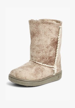 Botte beige mi-mollet avec une surface texturée, présentant des taches brunes et un détail de couture en tresse sur le côté. La semelle en caoutchouc offre adhérence et durabilité.