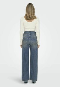 Breda blå denimjeans med hög midja, fem fickor och en urtvättad finish. Matchas med en långärmad krämfärgad topp. Enfärgad textur.