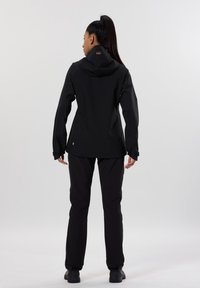 Veste imperméable noire avec capuche, manches longues et poignets réglables. Associée à un pantalon noir et des chaussures noires. Design simple et fonctionnel.