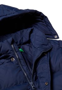 Giacca puffer blu navy con chiusura a zip e bottoni a pressione, dotata di colletto imbottito, texture liscia e etichetta verde all'interno.