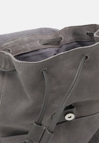 Szary zamszowy worek na ramię o miękkiej fakturze, z regulowanym ściągaczem i srebrnymi detalami. Wnętrze wykonane jest z ciemnej tkaniny.