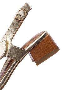 Zlatá kovová kožená sandále s nastavovacím páskem na přezku a středně vysokým blokovým dřevěným podpatkem na bílém pozadí.