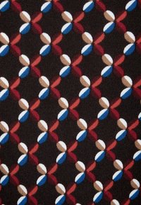 Textile avec un motif répétitif de formes rouges, bleues, marron et blanches sur un fond sombre, créant un design géométrique avec une texture douce.