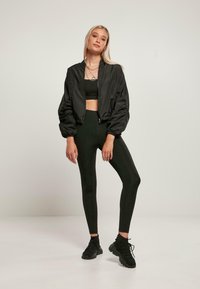 Black bomber jacket with puffed sleeves, cropped design. Paired with black leggings and footwear. Smooth fabric, minimal detailing.