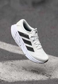 Witte sportieve schoen met een gestructureerde bovenkant en grijze accenten, met een ontwerp van drie strepen en een gevoerde zool. Lichtgewicht en ademende materialen.