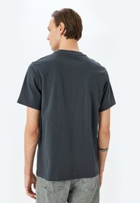Camiseta corta gris de algodón, con cuello redondo, dobladillo recto y una textura suave; combinada con unos jeans claros de mezclilla con estampado.