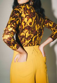 Maglione a maniche lunghe giallo con motivo floreale marrone e rosso, abbinato a pantaloni gialli a vita alta con tasche posteriori.