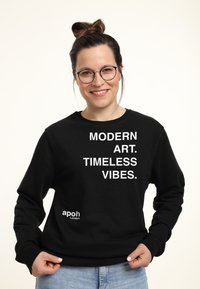 Felpa nera con testo bianco: "ARTE MODERNA. VIBRAZIONI ETERNE." Presenta polsini e orlo a costine, etichetta del marchio sul fronte, texture morbida.