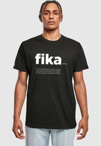 Juodas medvilninis T-shirt su ryškiais baltais žodžiais „fika“ priekyje, su mažesniu aprašymu apačioje. Trumpomis rankovėmis, su apvaliu kaklu.