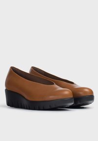 Zapatos de cuña de cuero marrón con punta redondeada, que cuentan con una suela de goma negra con borde dentado y un diseño de corte bajo en el tobillo.