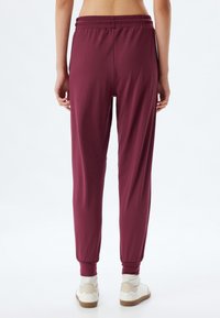 Bordeaux joggers met een elastische tailleband en boorden aan de enkels, gemaakt van een gladde stof, gecombineerd met witte en beige sneakers.