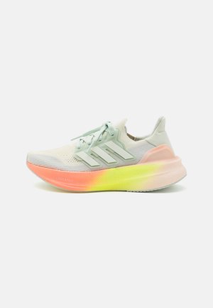 Zapatilla de running ligera con parte superior de punto blanca, cordones y rayas verde pálido, y suela degradada en tonos naranja, amarillo y rosa.