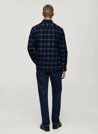 Camicia in flanella a quadri blu navy con maniche lunghe, polsini a bottoni e colletto classico, abbinata a jeans in denim scuri e scarpe nere.
