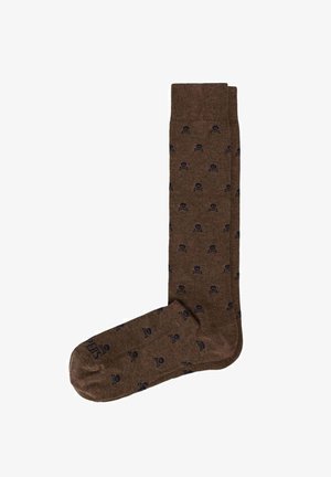 Chaussette marron montante jusqu'au genou avec de petits motifs noirs de tête de mort et os croisés partout et un texte près de la zone des orteils.