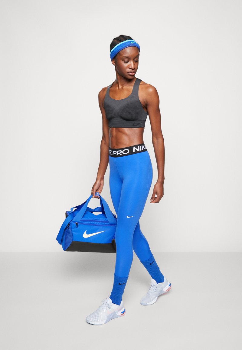 Fekete sportmelltartó, kék, magas derekú leggings Nike logóval, fehér sportcipők, kék tornazsák és hozzá illő fejpánt. Simító anyag, testhez simuló dizájn.
