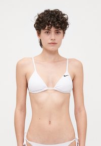 Biela bikiny s trojuholníkovými košíkmi a tenkými popruhmi. Obsahuje nariasenie a malé čierne logo Nike na ľavom košíku. Mäkká tkanina.