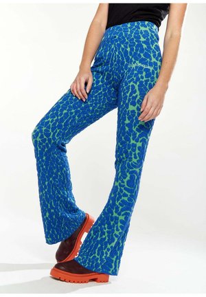 Blue and green patterned flared pants with textured fabric, featuring a vibrant animal print and a high waistband, paired with chunky orange heels.