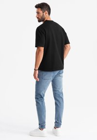 Camiseta negra de manga corta, material de algodón, corte relajado, combinada con jeans ajustados de color azul claro y zapatillas blancas. Diseño minimalista.