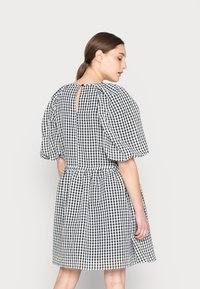 Vestido em padrão vichy preto e branco com mangas bufantes, cintura elástica e detalhe de recorte nas costas, feito de um tecido leve.