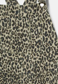 Beige en zwarte spijkeroveralls met luipaardprint, voorzien van verstelbare schouderbanden, voorzakken en een gestructureerd oppervlak.