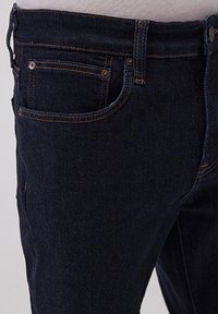 Dunkelblaue Jeans aus Denim mit taillierter Passform, klassischem Fünf-Taschen-Stil und goldenen Nähten entlang der Nähte und Taschen.