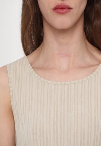 Top bej fără mâneci, cu textură ribdată verticală și decolteu rotunjit, având un luciu subtil și țesătură moale la contactul cu pielea.