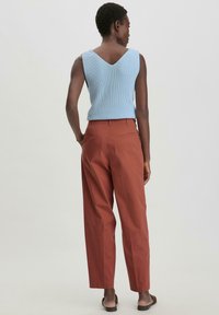 Vaaleansininen, ribattu, ilman hihoja oleva toppi V-pääntiellä yhdistettynä ruosteenvärisiin, korkeavyötäröisiin, leveälahkeisiin housuihin ja litteisiin sandaaleihin.