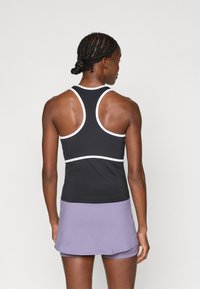 Fekete sporttank top, fehér díszítéssel és racerback kialakítással, lilás szoknyával párosítva, amely réteges szegéllyel és puha textúrával rendelkezik.