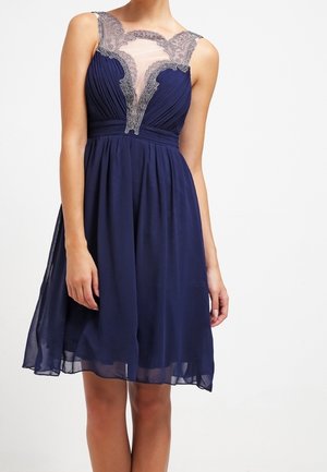 Robe sans manches bleu marine longueur genou avec jupe plissée et empiècement en dentelle transparente sur la poitrine et les épaules.