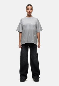 Szara, oversize koszulka z teksturowanymi plamami farby, połączona z czarnymi, szerokimi dżinsami z akcentami szwów i luźnym krojem.