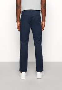 Chinos blu navy con design a gamba dritta, realizzati in tessuto morbido. Presentano tasche posteriori e sono abbinati a sneaker bianche.