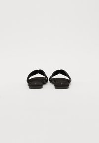 Sandale plate negre, cu un brad de piele întinsă și un design cu bretele crisscross. Vederea din spate arată o formă minimală și margini uniforme.