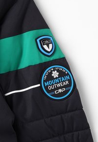 Manche de veste rembourrée noire et verte avec deux patches de la marque CMP, l'un en forme de bouclier et l'autre rond avec un flocon de neige et le texte "Mountain Outwear".