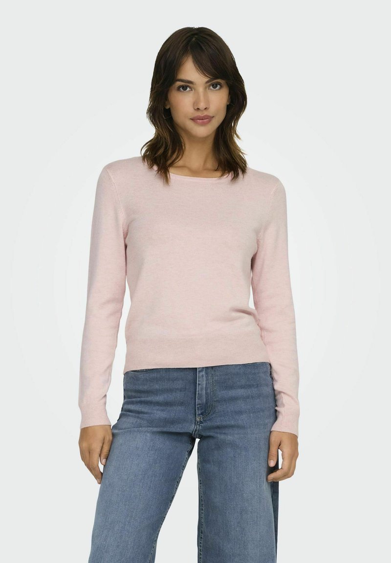 Pull long à manches longues rose clair avec un col rond, fabriqué dans un tissu doux, associé à un jean en denim bleu.