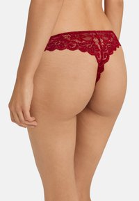 Vrouw in een rood bloemen kanten stringondergoed, gezien van achteren, met de nadruk op het ingewikkelde kantontwerp en de huidtextuur.