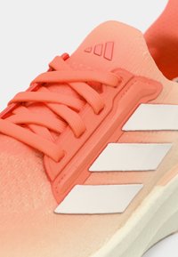 Koralle atletiske sko med struktureret stof, hvidt tre-stribes design, strukturerede snørebånd og en polstret krave for komfort.