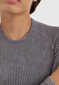 Sivi rebrasti materijal s okruglim izrezom; sadrži suptilne svijetle i tamne pruge te raglan rukave s završnim šavovima.