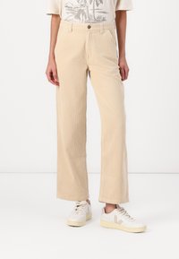 Beige corduroy wide-leg pants with vertical ribbing, featuring a high waist, front pockets, and a smooth texture. Paired with white sneakers.