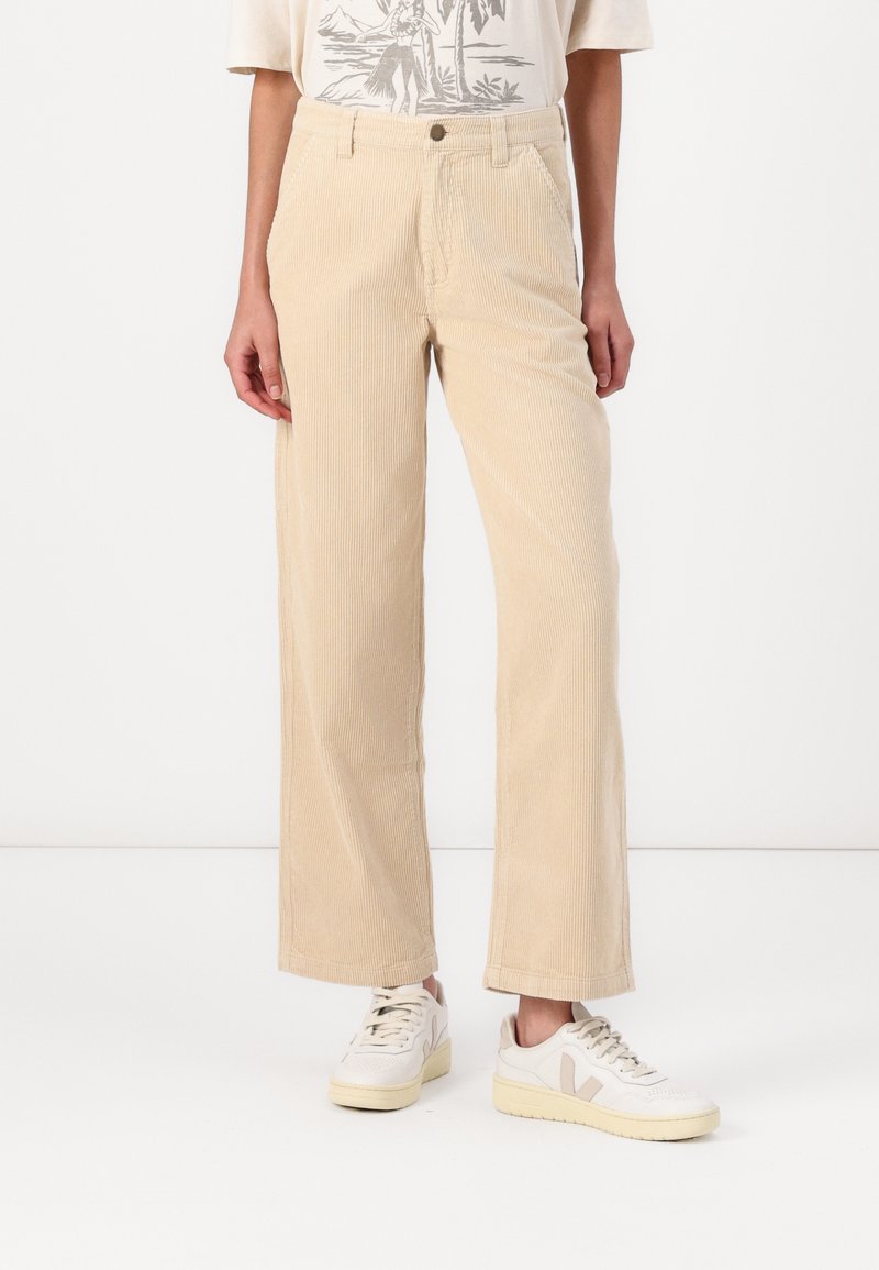 Beige corduroy wide-leg pants with vertical ribbing, featuring a high waist, front pockets, and a smooth texture. Paired with white sneakers.