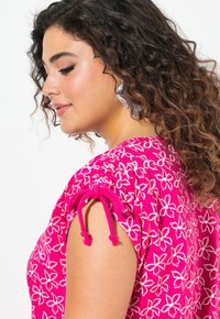 Vestido de patrón floral en tono rosa con detalles de cordón en las mangas y un corte holgado. Fabricado con material ligero de textura suave.
