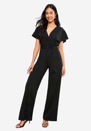 Combinaison noire avec des manches courtes en volants, un décolleté en V profond, une ceinture à nouer à la taille et un pantalon à jambes larges. Texture de tissu lisse.