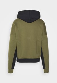 Huvtröja i olivgrön tyg med svarta detaljer på ärmarna och nederkanten. Mjuk textur, avslappnad passform.