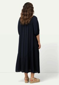 Laivansinis maxi-mekko, virtaava malli kerroksellisella helmalla, lyhyet hihat ja tekstuurinen kangas. Yhdistetty beigeihin espadrillesandaaleihin.