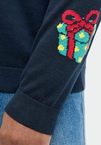 Navy sweater featuring a green, yellow-spotted gift graphic with a red bow on the left sleeve. Ribbed cuff and smooth texture.