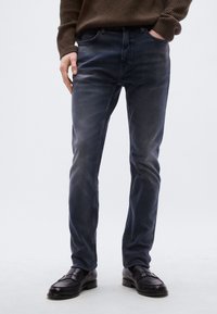 Mørkeblå jeans i denim med rett passform, fem lommer og subtil falming. Brukt med svarte skinnloafers.