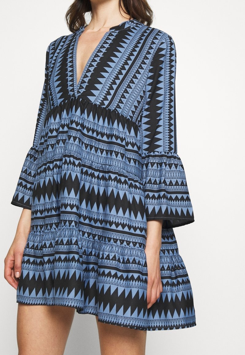 Robe à motifs géométriques bleu et noir avec un décolleté en V profond, des manches évasées et une jupe évasée, réalisée dans un tissu léger.