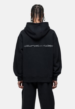Black oversized hoodie with a drawstring, featuring white cursive text "Good For Nothing" on the back, made from soft cotton material.