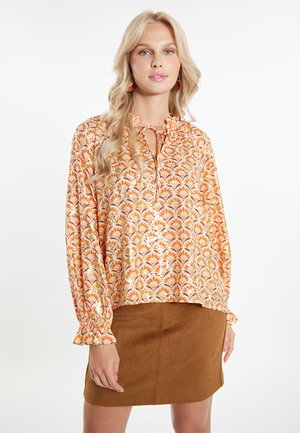 Bluză cu mânecă lungă, de culoare portocalie, cu un model floral, având un decolteu legat cu fundă și mansete franjurate, asortată cu o fustă din suede maro.