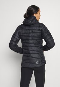 Black puffer jacket with horizontal quilting, attached hood, and a sleek silhouette. Features subtle logo detail at the hem.